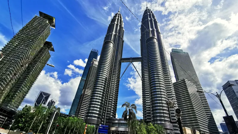The Petronas Towers rising above palms and city buildings under a blue sky