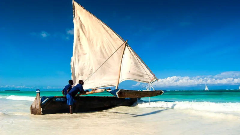 A dhow with its sail up on the turquoise shallows off Zanzibar
